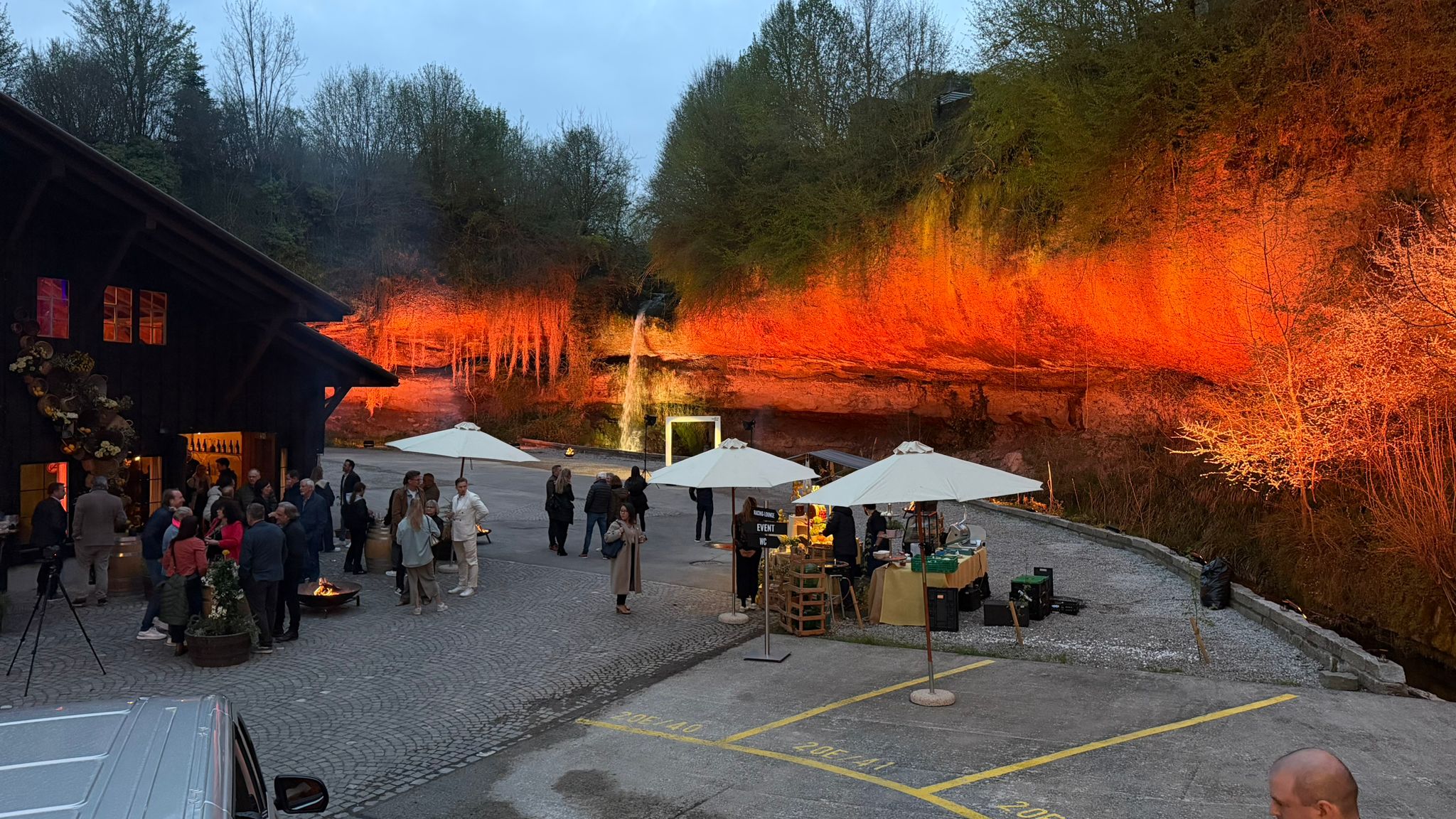Eventdesign: Innenhof am Abend mit orange beleuchteten Bäumen, Sonnenschirmen und Gästen, Firmenevent in Zürich