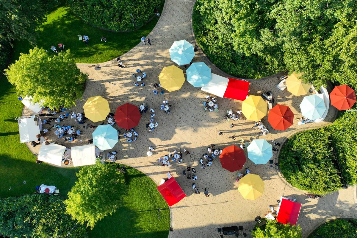 Aerial view of a summer party in a park with colourful parasols, market stalls and guests: event design and company event in Zürich