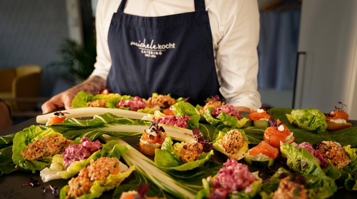 Koch in michele-kocht-Schürze hinter einem Brett mit Häppchen auf Salatblättern, Firmenapéro in Zürich