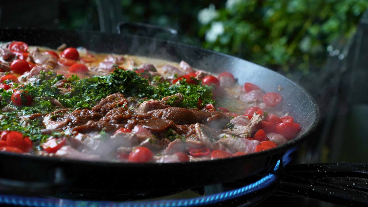 Live cooking: meat, cherry tomatoes and parsley in a large pan over a blue flame, Zürich event catering