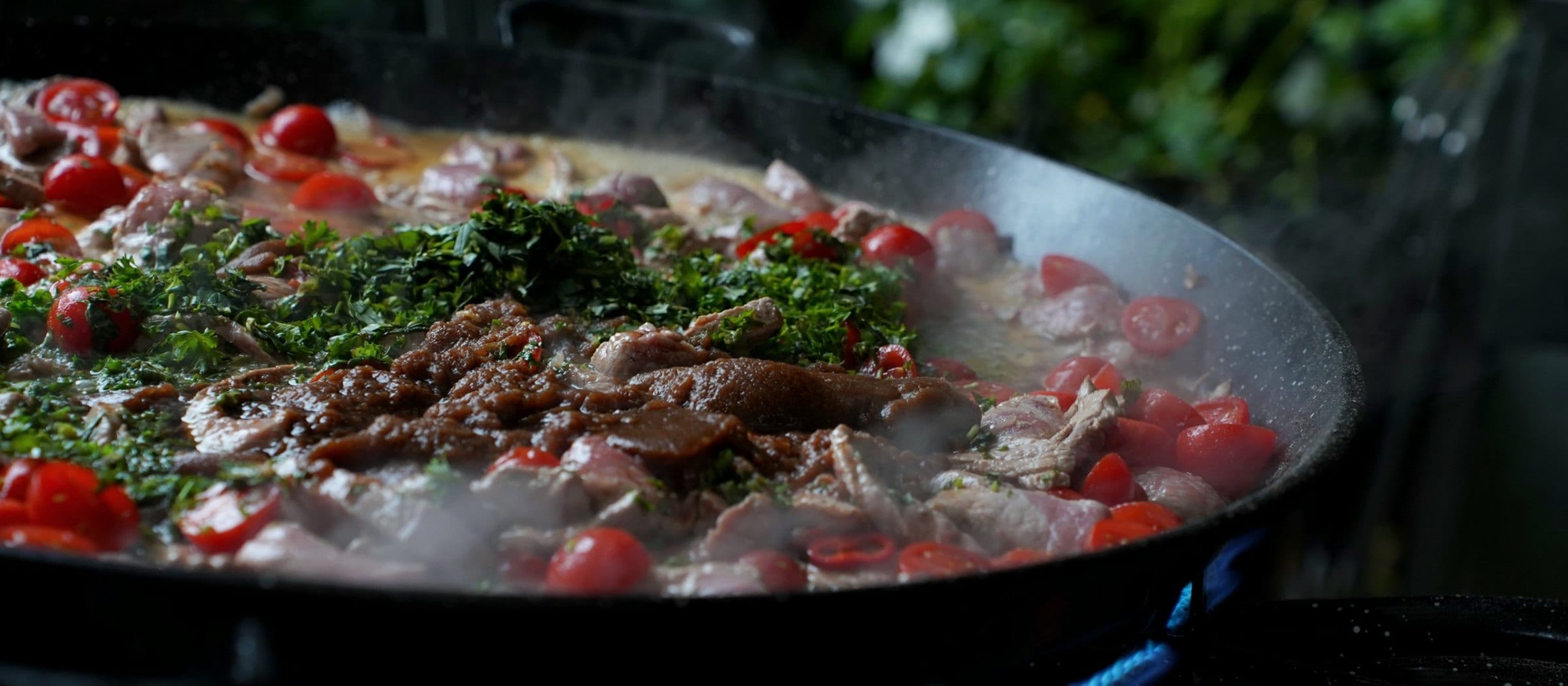 Fleisch, Kirschtomaten und Petersilie in der Pfanne über blauer Flamme: Menüs von MicheleKocht Zürich