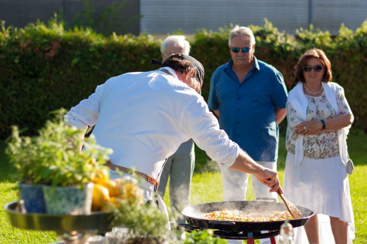 Michele stirring the steaming paella pan as guests watch in the garden: live cooking in Zürich