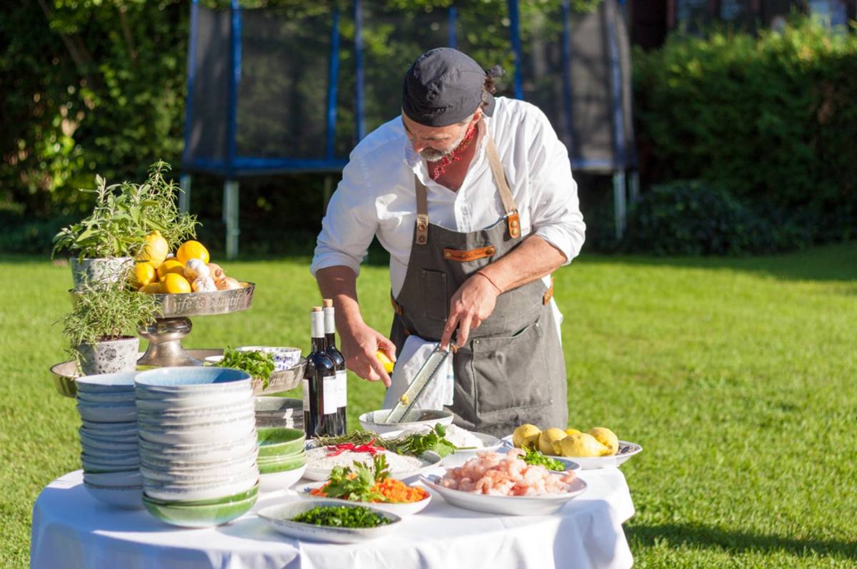 Michele grating lemon over a table of prawns and herbs in the garden: live cooking, Zürich catering