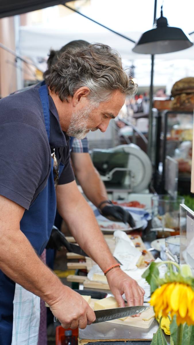 Michele cutting cheese for apéro boards at the market stall, a live station in Zürich