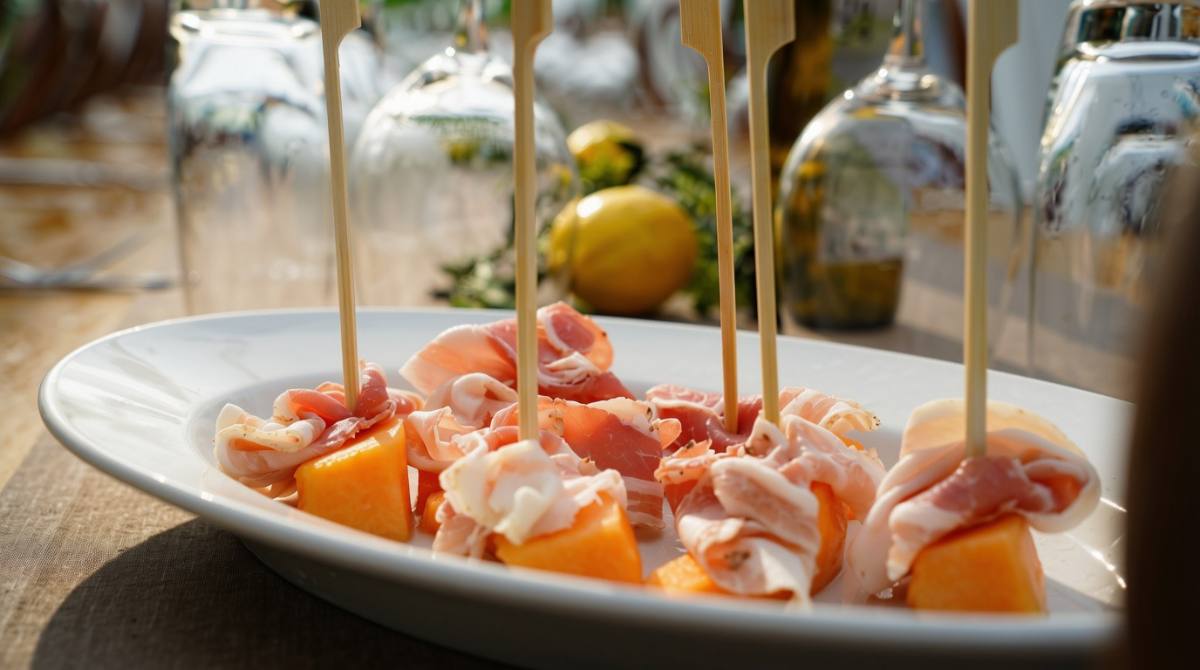 Melon wrapped in prosciutto on skewers, glasses and lemons behind: tavolata antipasti, Zürich catering