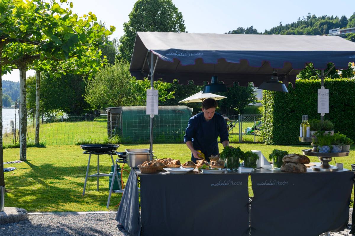 Tavolata station under the michele kocht canopy in a lakeside garden: a chef setting out bread, herbs and antipasti, catering from Zürich